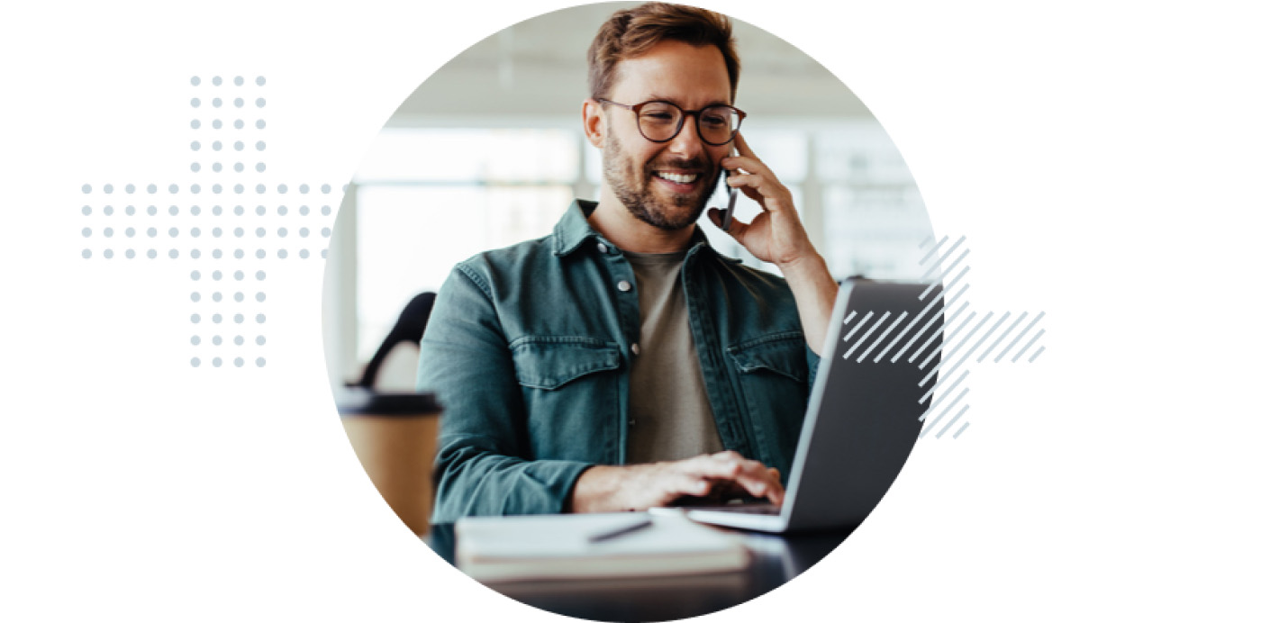 A man engaged in a phone conversation while seated in front of a laptop.
