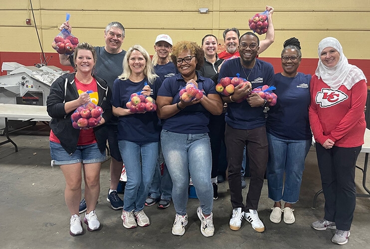 A group of multi-ethnic Empower employees pose holding bags of apples