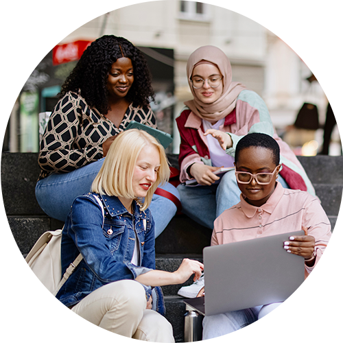 A group of female students sit on steps viewing laptop
